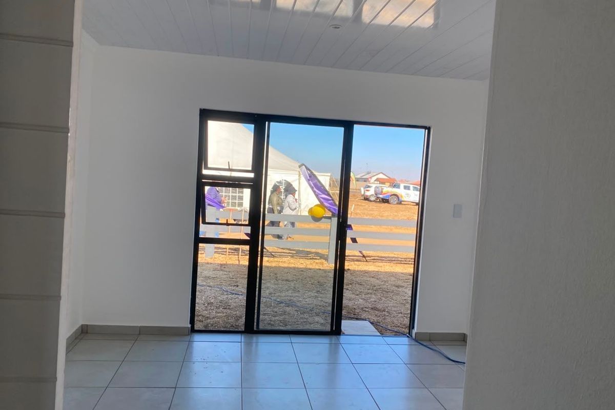 A bright, empty living area featuring neutral tiled flooring, a modern tongue and groove ceiling, and a large sliding glass door leading outdoors.