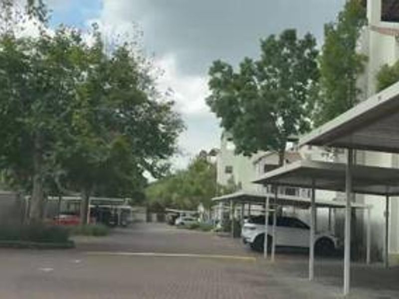Exterior view of the apartment complex featuring paved driveway access and multiple covered parking bays surrounded by established trees.