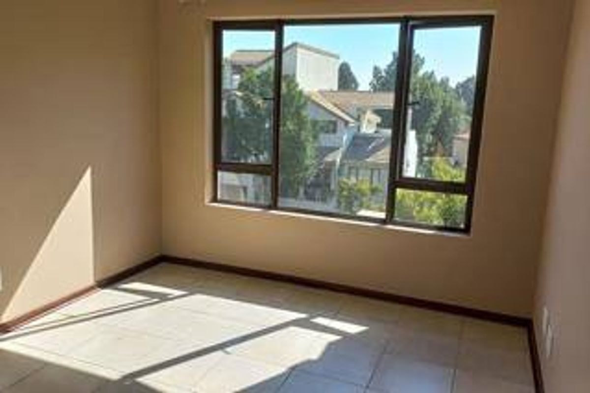 A bright, empty bedroom featuring neutral wall tones, tiled flooring, and large aluminium-framed windows allowing for ample natural light.