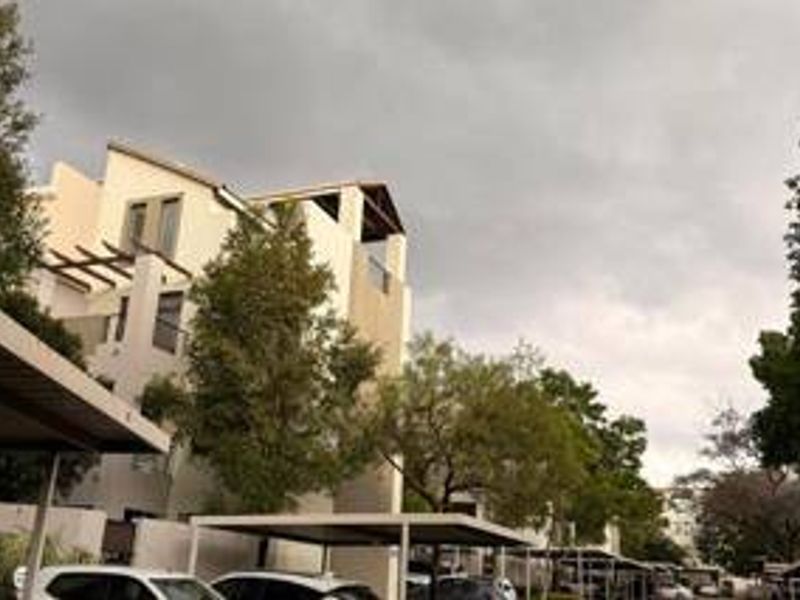 Exterior view of a multi-story apartment complex featuring covered parking carports and upper-level balconies with pergola structures.