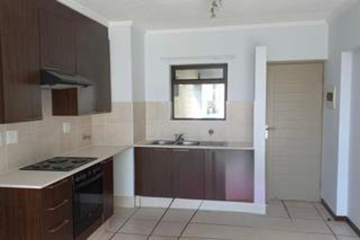 A functional kitchen featuring dark wood cabinetry, built-in oven and hob, tiled splashbacks, and a double basin sink.