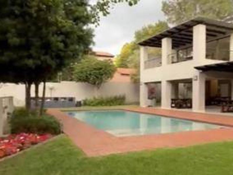 A well-maintained outdoor area featuring a swimming pool, paved surround, and a two-story residence with a covered patio and balcony.