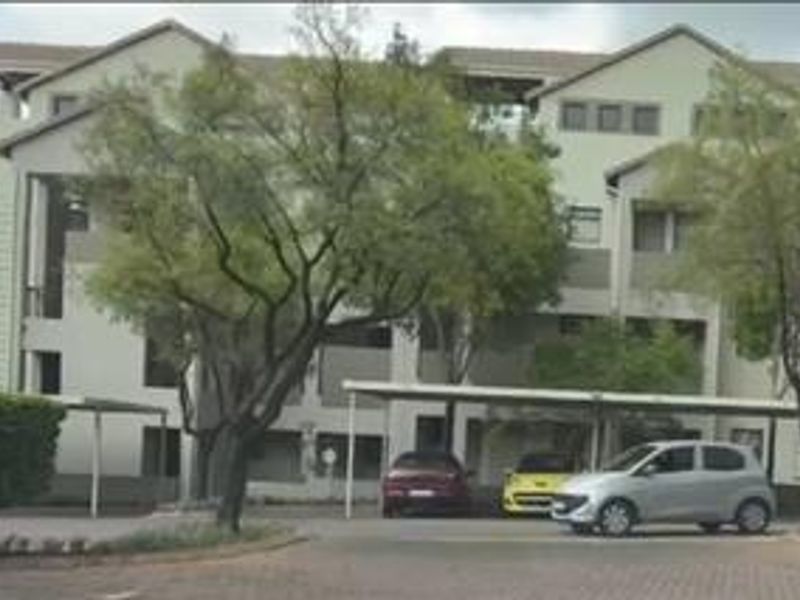 Front elevation of a multi-story apartment complex featuring covered parking bays and paved driveway access.