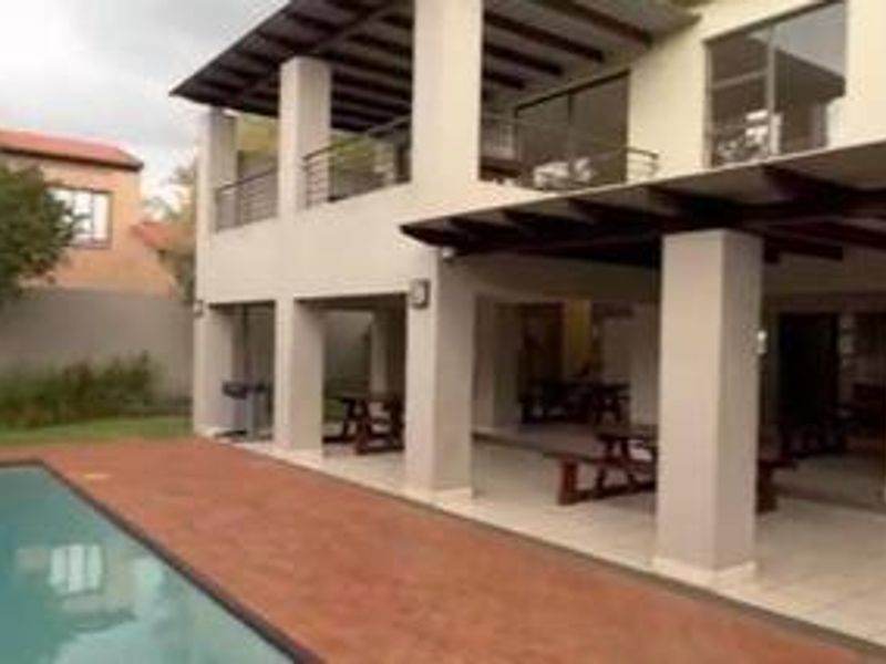 A spacious outdoor pool area featuring a large swimming pool, a tiled deck, and a covered patio with structural pillars.