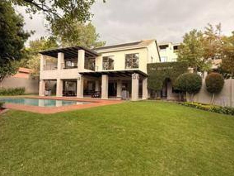 Rear view of the property featuring a spacious lawn, swimming pool, and a covered patio area with an upper-level balcony.