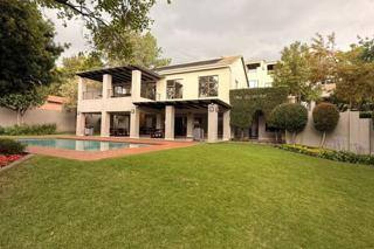 Rear view of the property featuring a spacious lawn, swimming pool, and a covered patio area with an upper-level balcony.