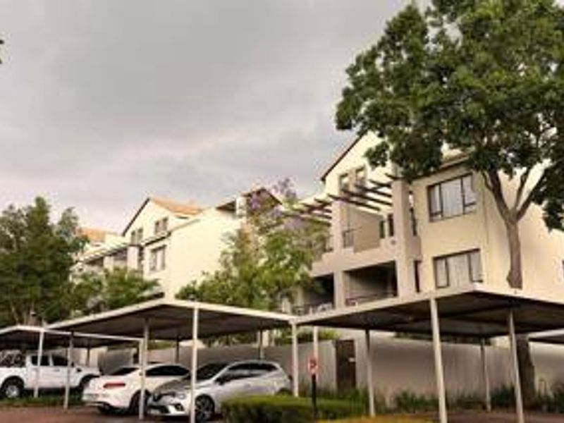 Exterior view of an apartment complex featuring covered parking bays and balconies with pergola structures.