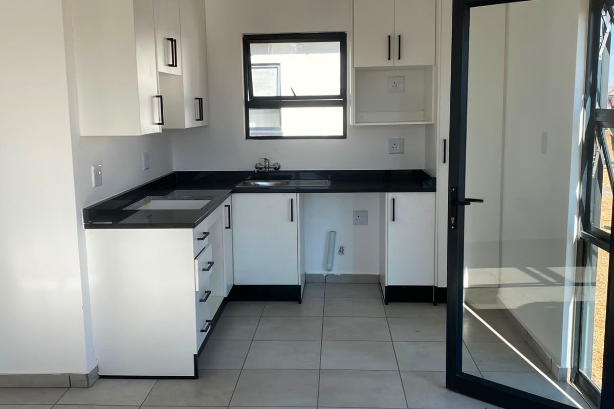 A clean, modern kitchen featuring white cabinetry, black countertops, tiled flooring, and direct access to the outdoors through a glass door.