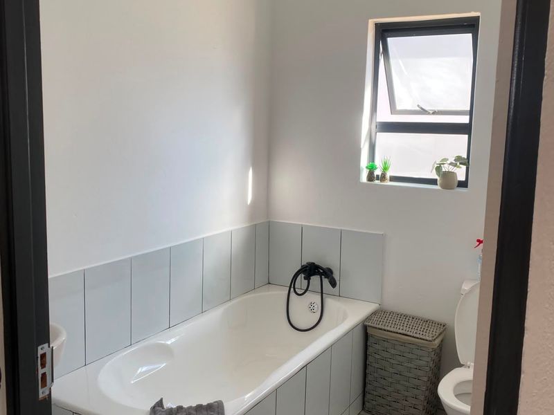A functional bathroom featuring a bathtub with tiled surround, a toilet, and a window providing natural light.