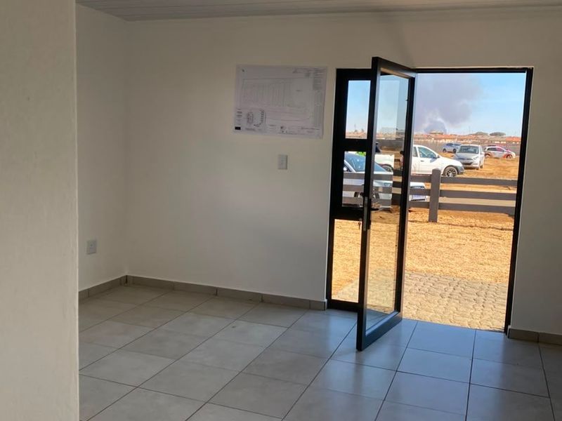 A bright, empty entrance area featuring neutral floor tiles, a modern glass door, and a clean tongue and groove ceiling.