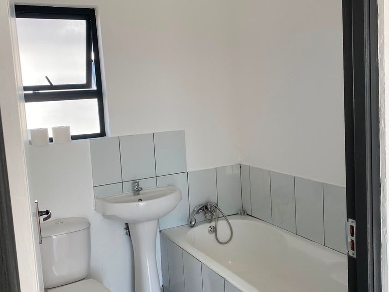 A functional bathroom featuring a pedestal basin, bathtub, toilet, and tiled finishes, offering a clean and simple layout.