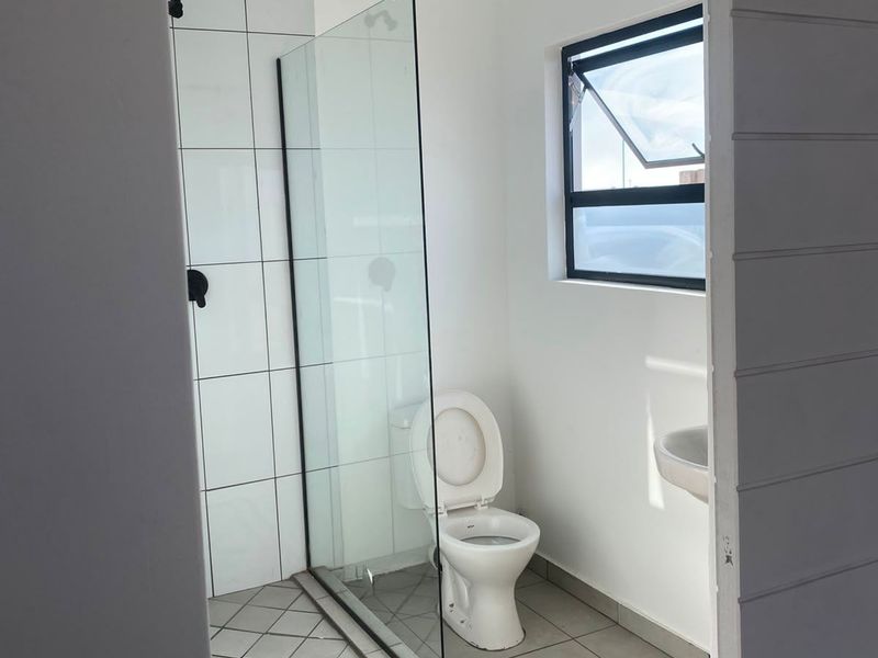 A clean, modern bathroom featuring a walk-in shower with a glass screen, a wall-mounted basin, and a toilet, finished with neutral floor and wall tiles.