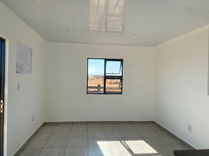 A bright, empty living area featuring neutral tiled flooring, a modern tongue and groove ceiling with recessed lighting, and a large aluminium-framed window.