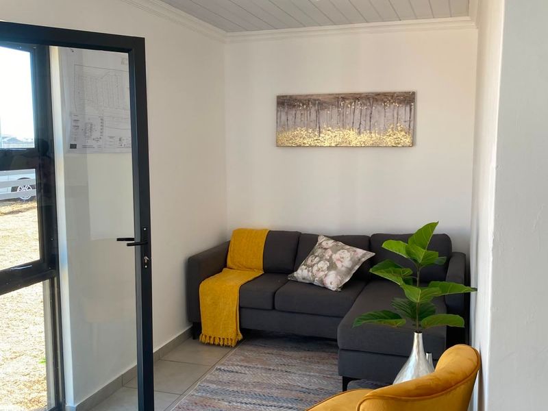 A bright living area featuring tiled flooring, a tongue and groove ceiling with recessed lighting, and a modern aluminium framed glass door.