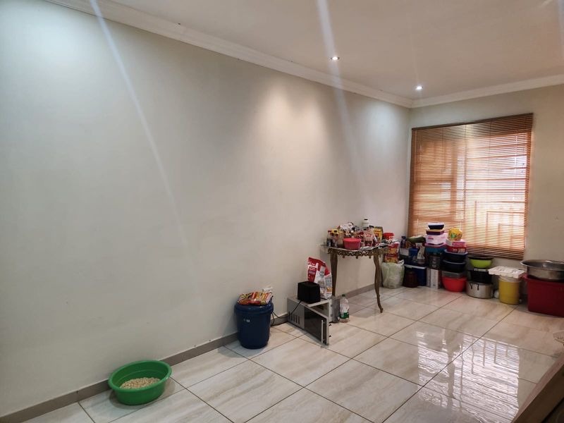 A bright, open living area featuring neutral tiled flooring, recessed downlighting, and wooden venetian blinds, offering a clean canvas for interior design.