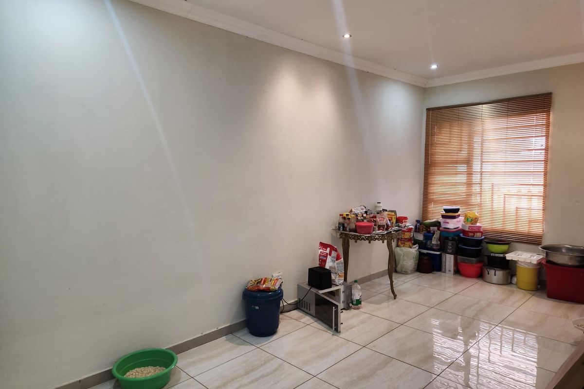 A bright, open living area featuring neutral tiled flooring, recessed downlighting, and wooden venetian blinds, offering a clean canvas for interior design.