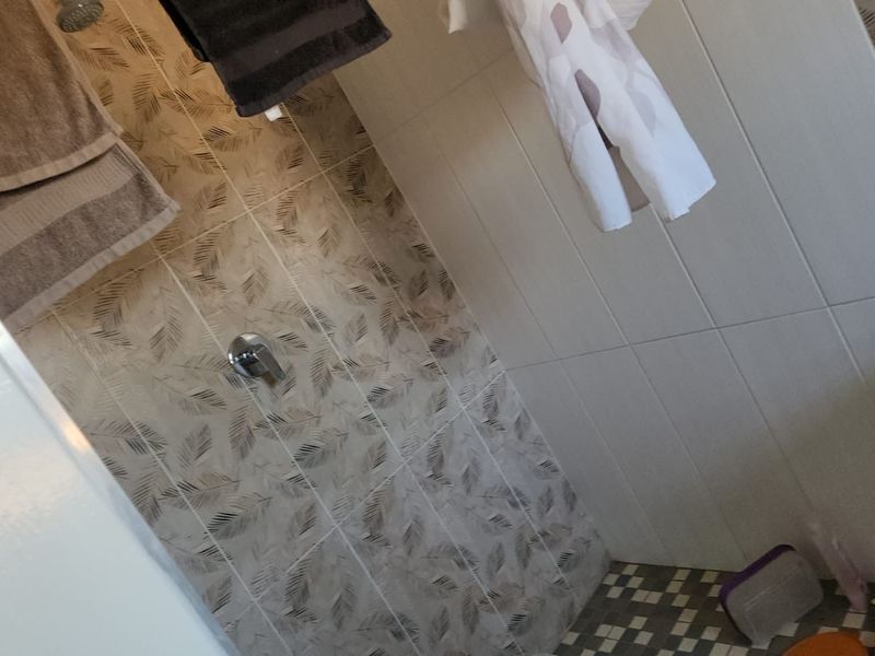 A bathroom shower area featuring patterned wall tiles and a tiled floor, equipped with a standard shower mixer and head.
