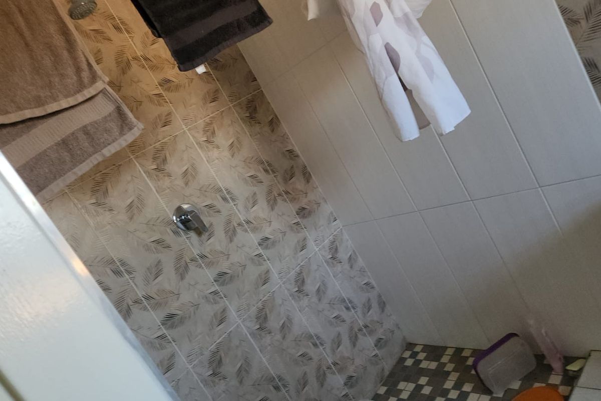 A bathroom shower area featuring patterned wall tiles and a tiled floor, equipped with a standard shower mixer and head.
