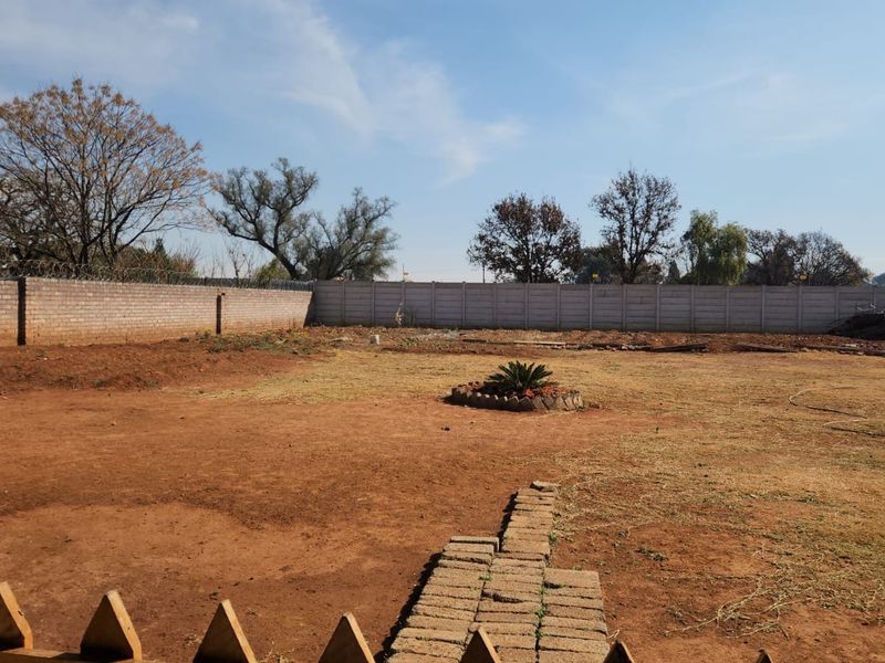 A large, open backyard area featuring a perimeter wall with security spikes and a central paved walkway, offering significant potential for landscaping.