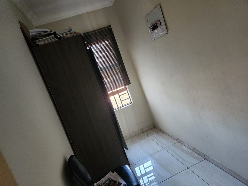 A small bedroom featuring tiled flooring, a window with fitted blinds, and a wall-mounted electrical distribution board.