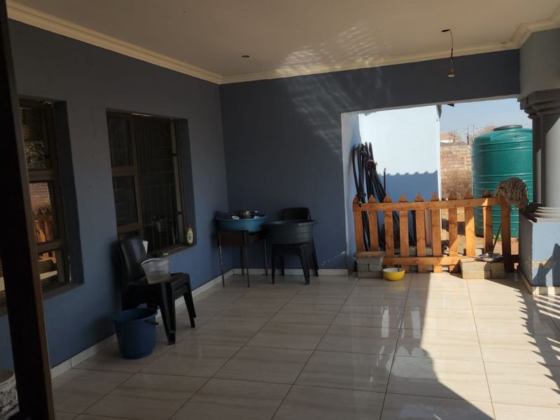 A covered patio area featuring tiled flooring, a concrete support pillar, and wooden perimeter fencing, with an adjacent water storage tank.