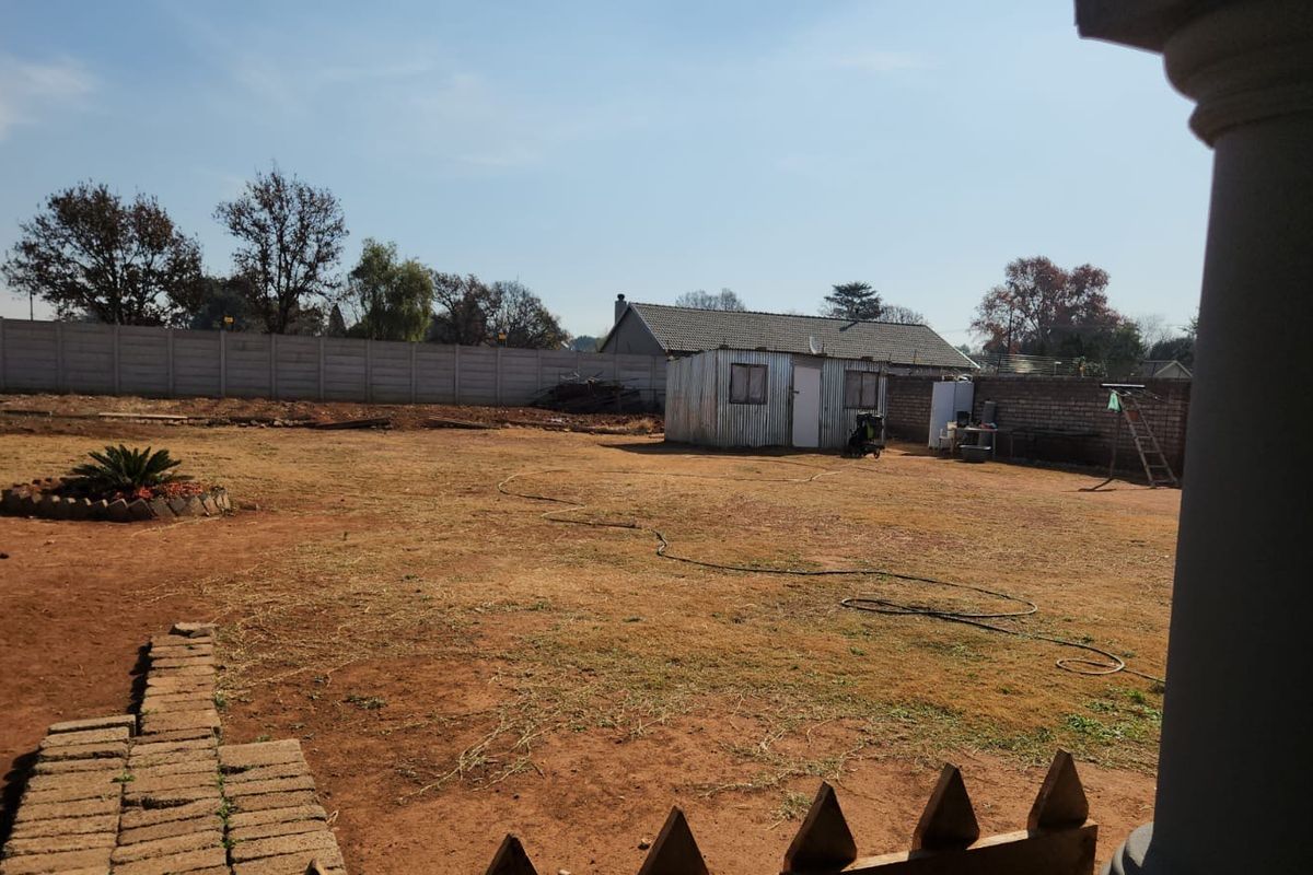 A spacious rear garden featuring a large open yard, a corrugated metal storage shed, and perimeter boundary walls.