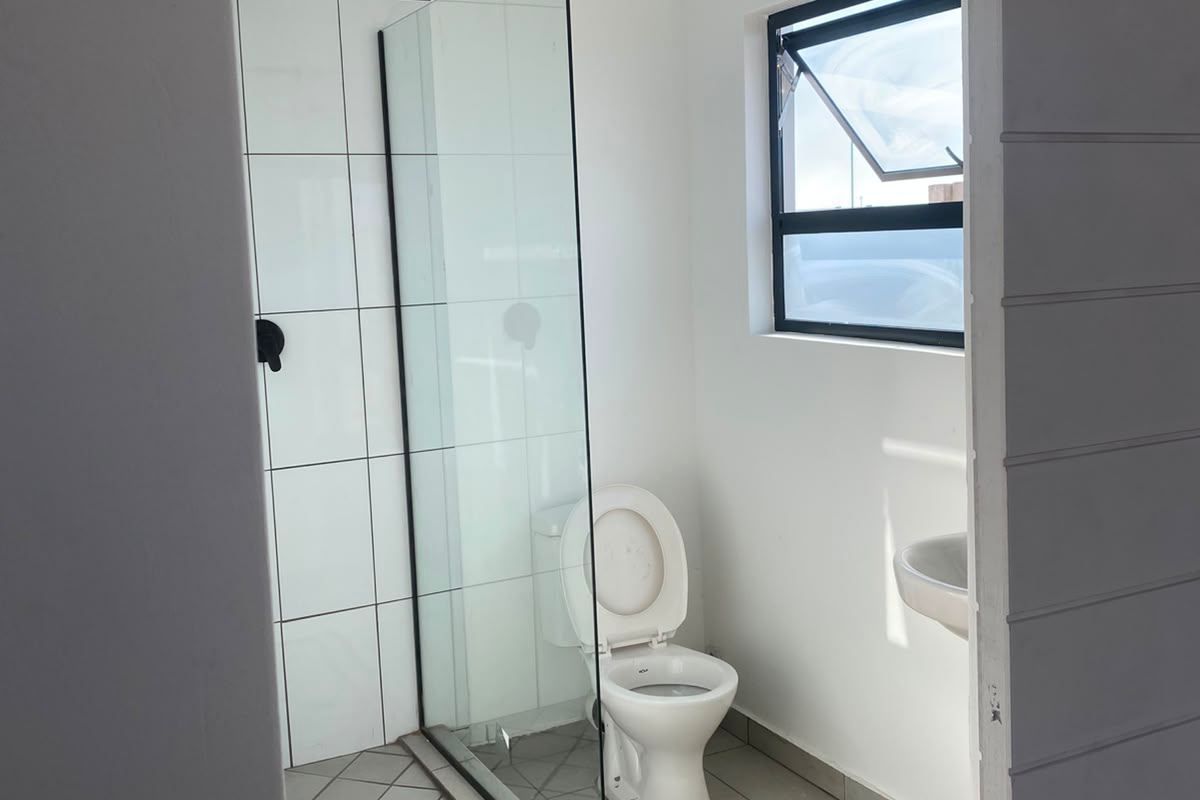 A clean, modern bathroom featuring a walk-in shower with a glass screen, a wall-mounted basin, and a toilet, finished with neutral floor and wall tiles.