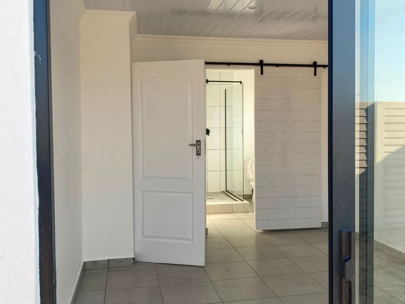 A bright, empty bedroom featuring tiled floors, a tongue and groove ceiling, and a sliding barn door leading to an en-suite bathroom.
