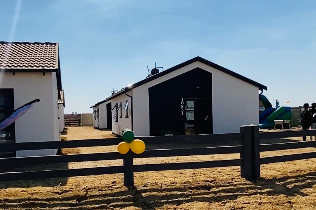 Front view of a modern single-story residential house featuring a contrasting black and white facade, tiled roof, and perimeter timber fencing.