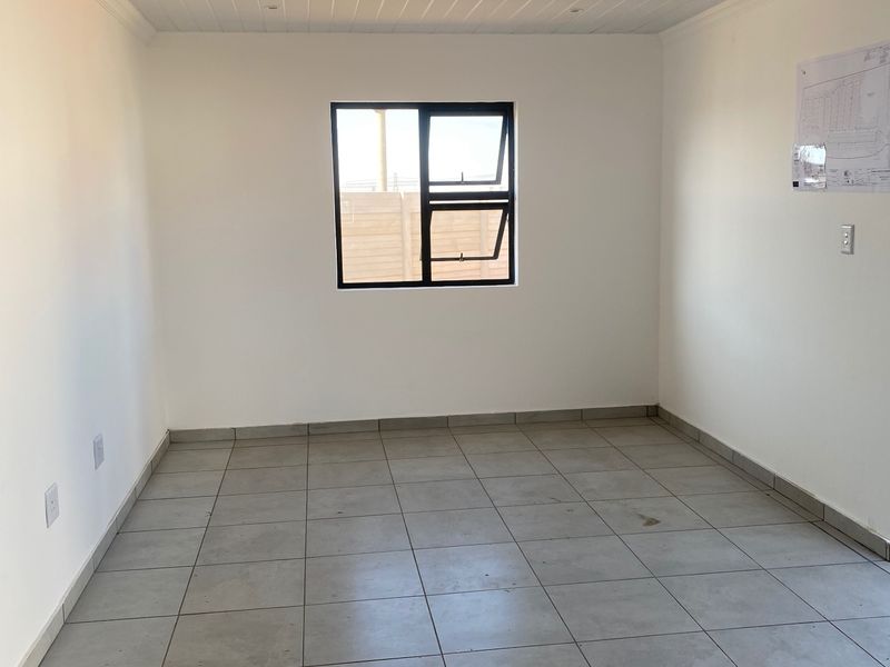 A clean, empty bedroom featuring neutral tiled flooring, white walls, and an aluminium-framed window, providing a versatile blank canvas for interior design.