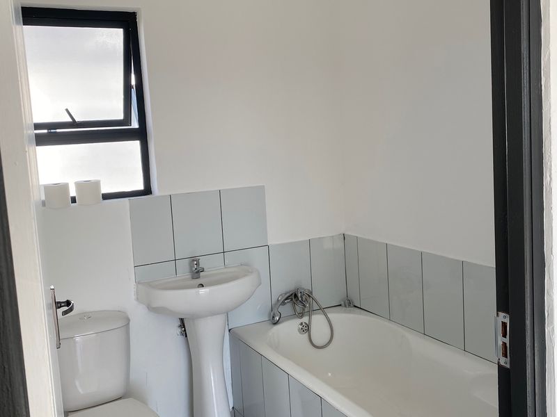 A functional bathroom featuring a pedestal basin, bathtub, and toilet with neutral wall and floor tiling.