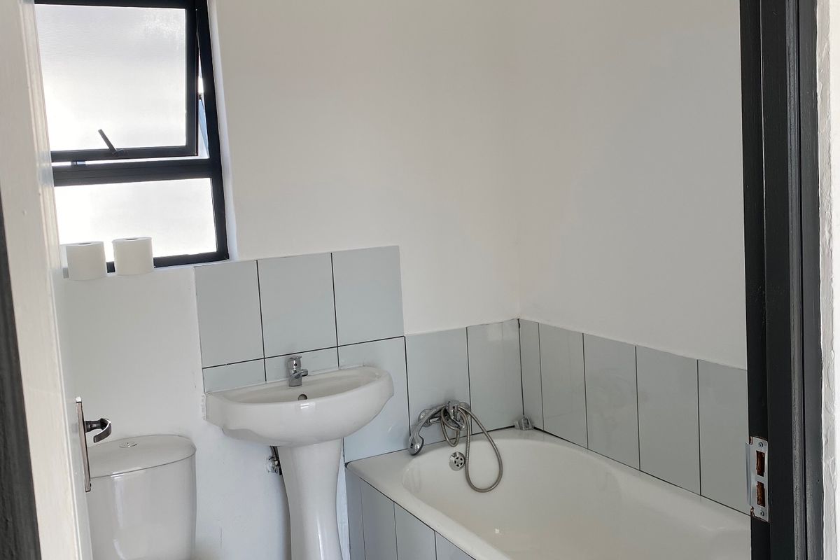 A functional bathroom featuring a pedestal basin, bathtub, and toilet with neutral wall and floor tiling.