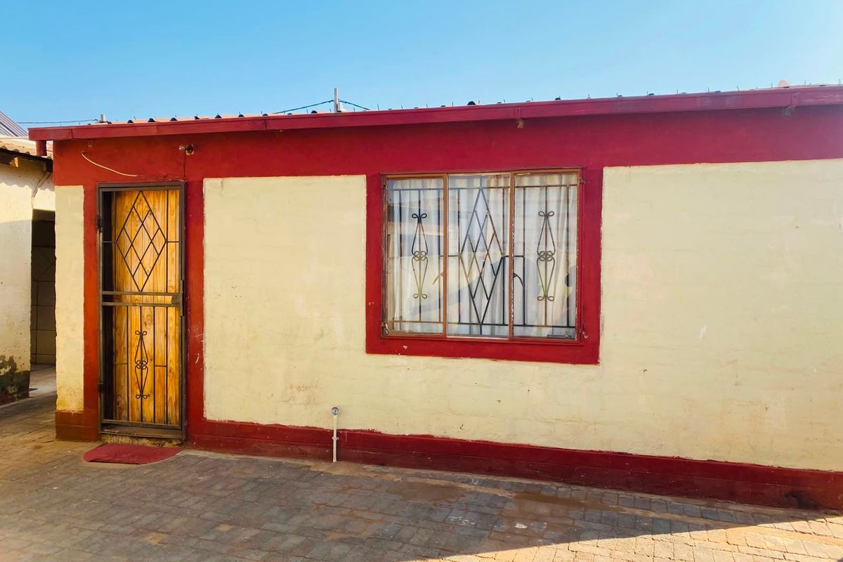 Rear exterior view of the property featuring a paved courtyard area, security gate, and window security bars.
