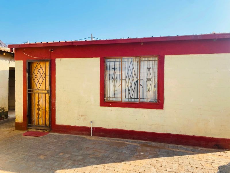 Rear exterior view of the property featuring a paved courtyard area, security gate, and window security bars.