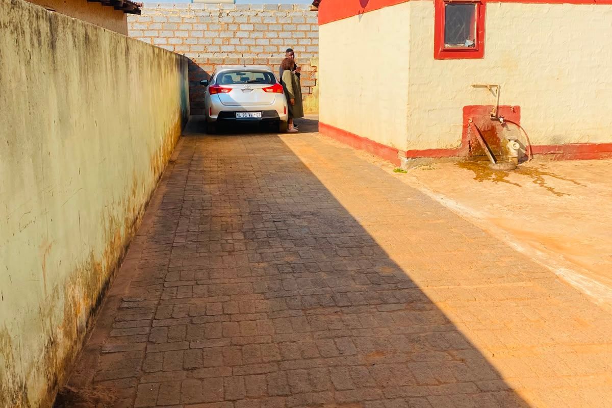 A paved rear driveway area featuring a boundary wall, an external water tap, and a satellite dish mounted on the building exterior.