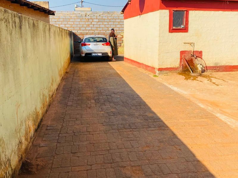 A paved rear driveway area featuring a boundary wall, an external water tap, and a satellite dish mounted on the building exterior.
