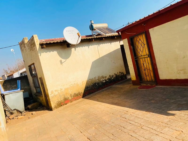 Rear exterior view of the property featuring a paved courtyard, solar water heating system, and security gate access.