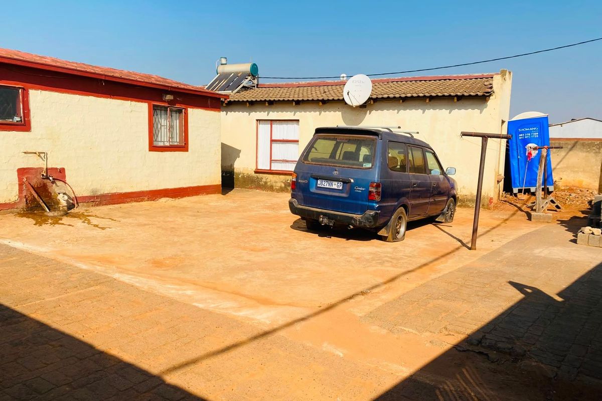 Rear exterior view of the property featuring a paved courtyard, solar water heating system, and satellite dish installation.