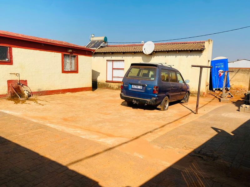 Rear exterior view of the property featuring a paved courtyard, solar water heating system, and satellite dish installation.