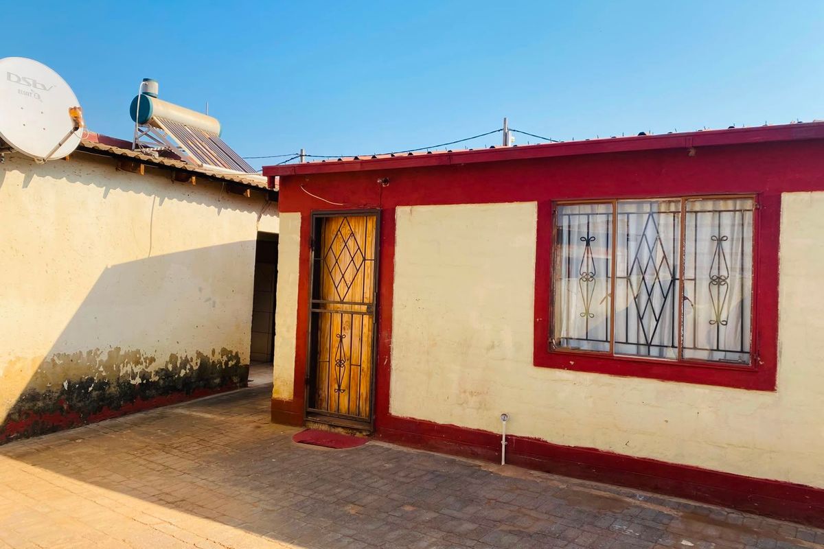 Rear exterior view of the property featuring a paved courtyard, security gates, and a solar water heating system installed on the roof.
