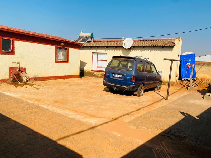 Rear courtyard area featuring paved ground, exterior wall access, and a solar water heating system installed on the roof.