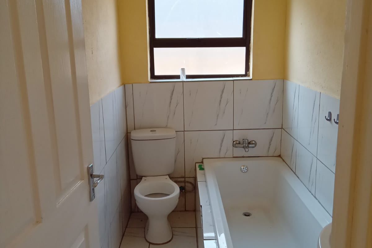 A compact bathroom featuring a built-in bathtub, toilet, and tiled finishes throughout, offering a functional space ready for potential cosmetic updates.