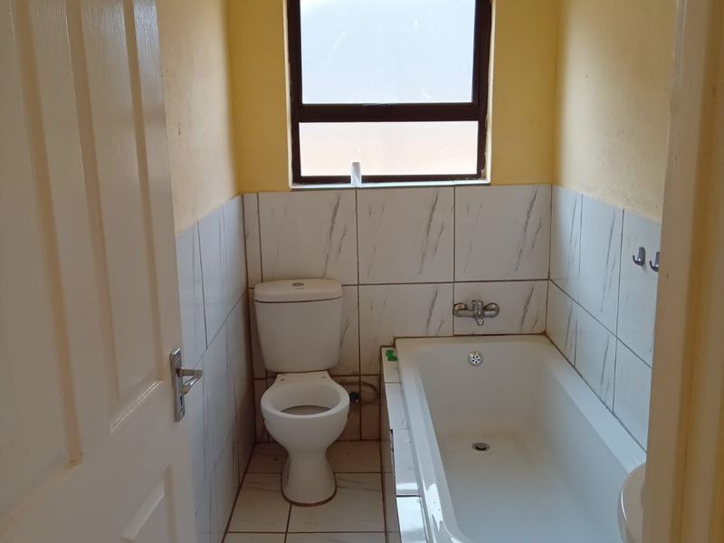 A compact bathroom featuring a built-in bathtub, toilet, and tiled finishes throughout, offering a functional space ready for potential cosmetic updates.
