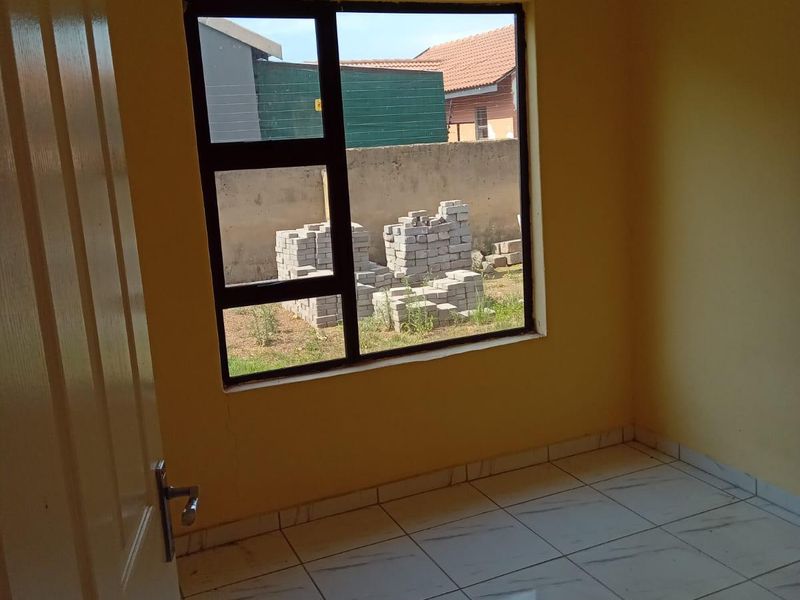 A vacant bedroom featuring tiled flooring, yellow painted walls, and an aluminium window frame overlooking the rear yard.