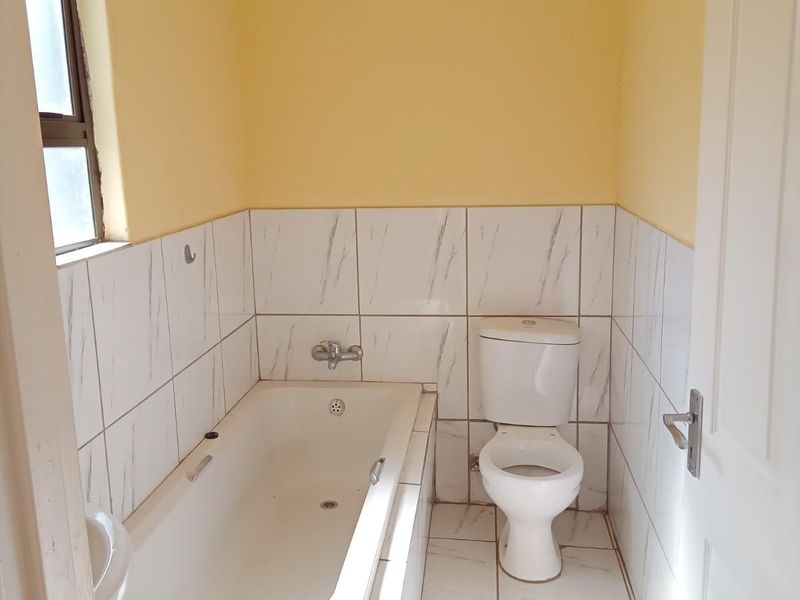 A functional bathroom featuring a built-in bathtub, toilet, and white marble-effect wall and floor tiles.
