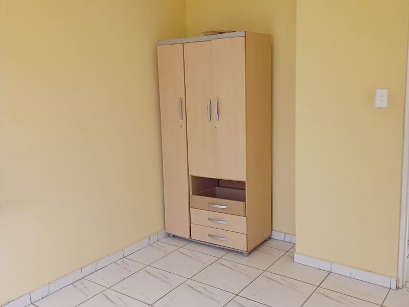 A simple bedroom featuring light-colored tiled flooring and yellow painted walls, providing a clean and neutral space ready for personalization.