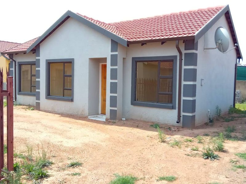 A modern single-story residential house featuring a tiled roof, painted plaster exterior, and aluminium window frames, set on an unpaved plot.