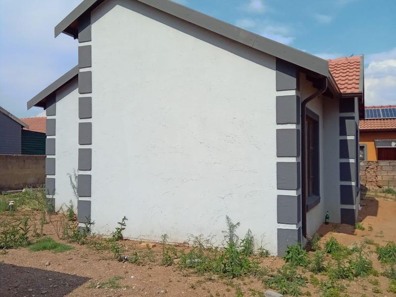 Side and rear view of a residential house featuring a tiled roof, painted exterior walls with decorative corner detailing, and an unlandscaped yard.