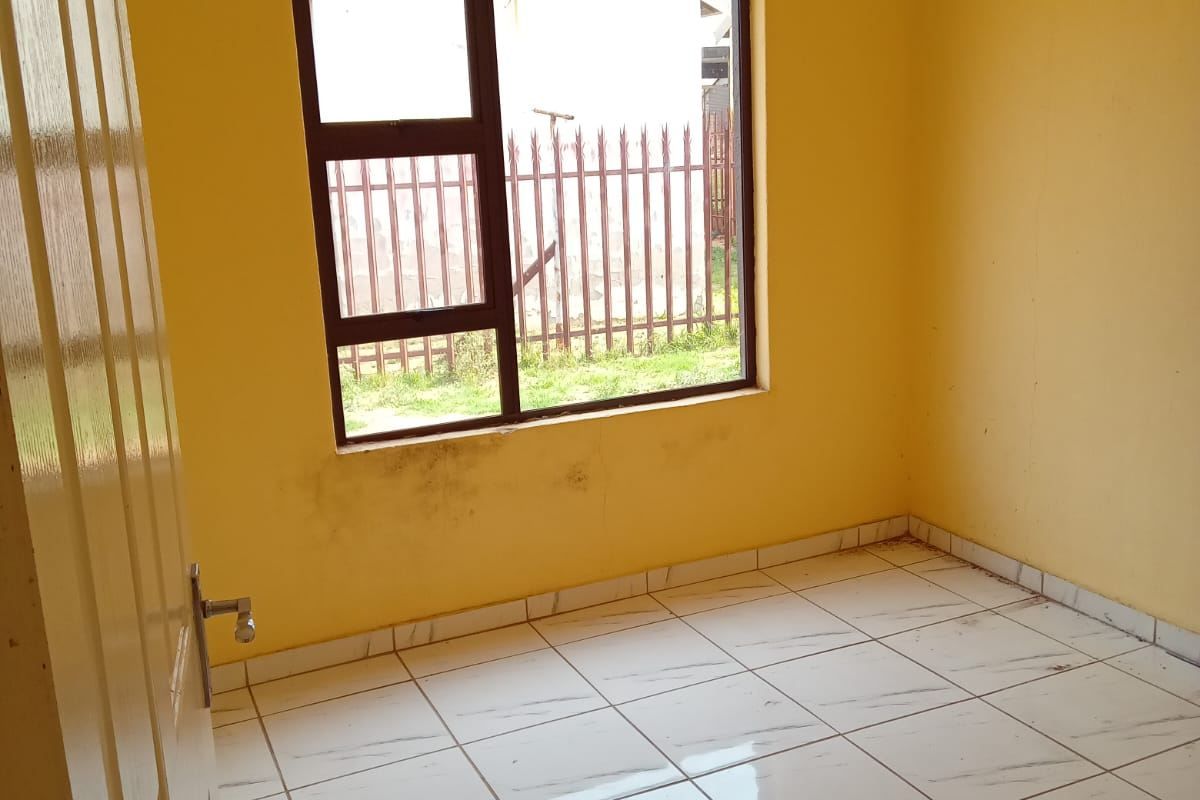An empty bedroom featuring tiled flooring and a metal-framed window, requiring minor cosmetic updates to the walls.