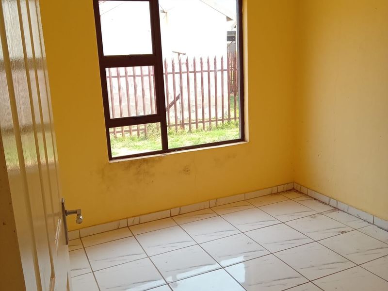 An empty bedroom featuring tiled flooring and a metal-framed window, requiring minor cosmetic updates to the walls.